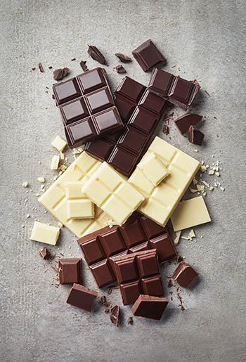 dark, white, and milk chocolate bars scattered on a gray background